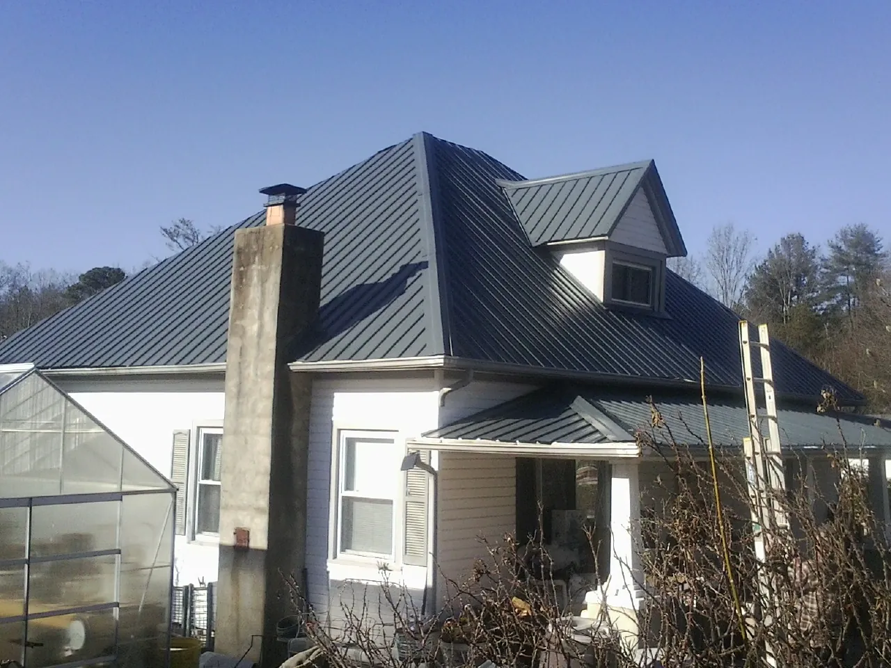 Dark blue standing seam metal roof on a white farmhouse with dormer — Slate & Tile Roof Repair by Roofing Brothers in Molena