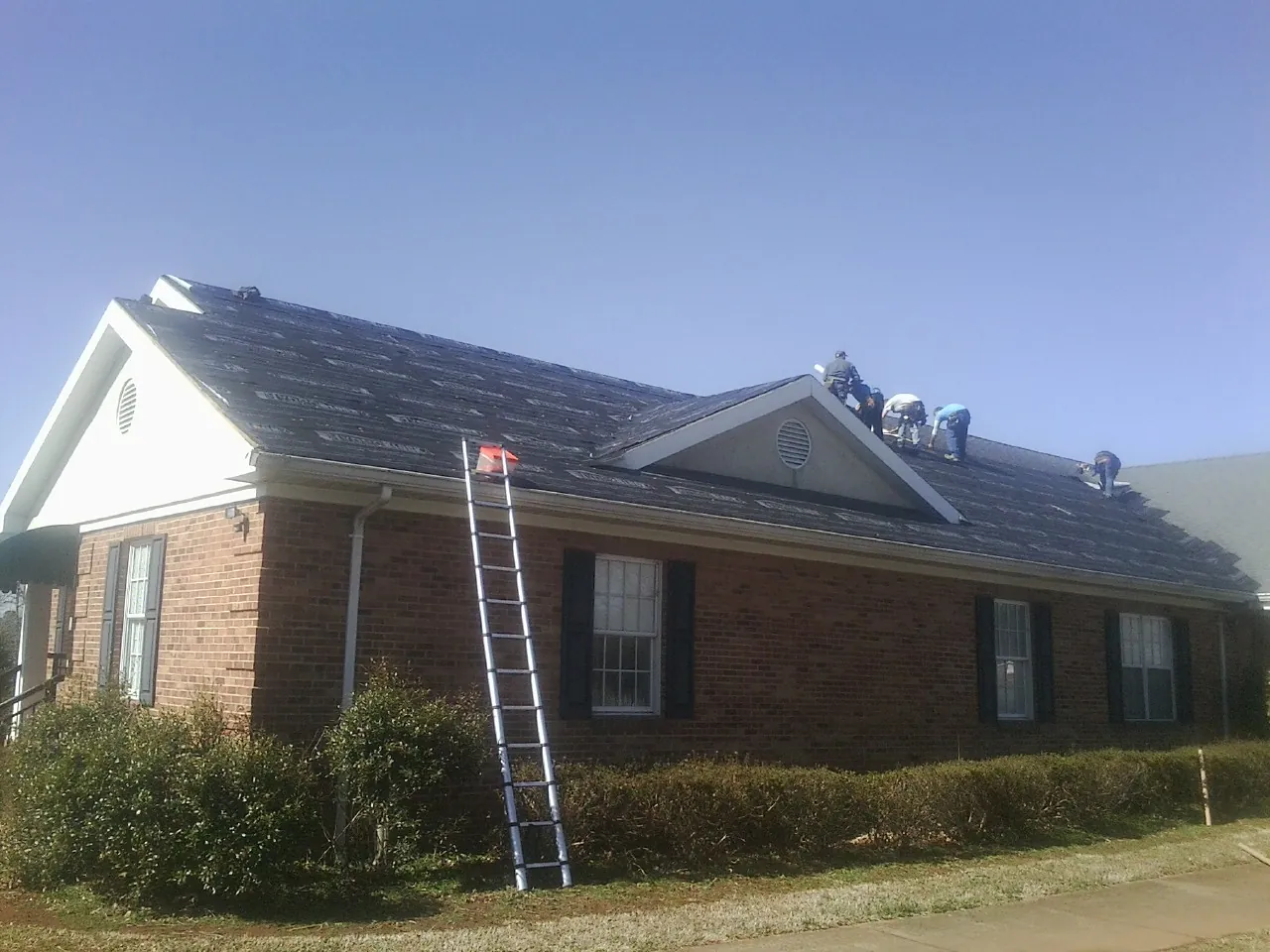 Crew tearing shingles off a brick ranch roof with a ladder set — Metal Roof Repair work by our crew in Molena