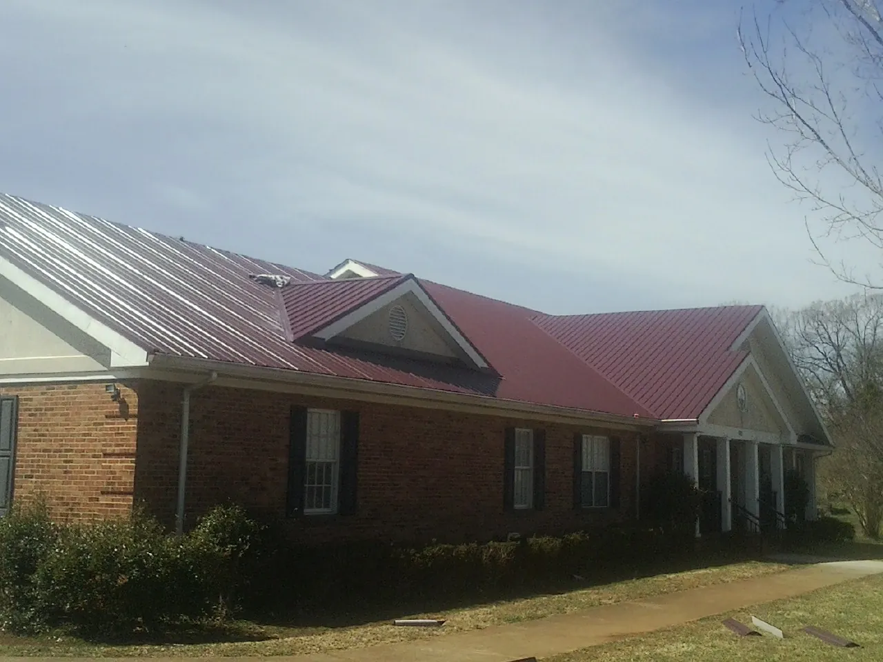 Red metal roof with gabled entries on a long brick building, from a Hail Damage Roof Repair job in Molena