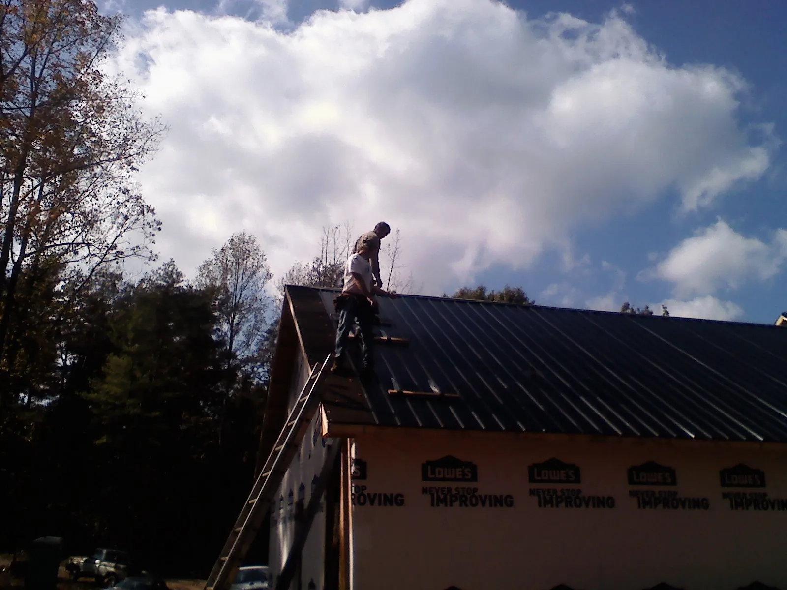 Roofer fastening dark metal panels high against a cloudy sky, from a Roof Inspection job in Molena