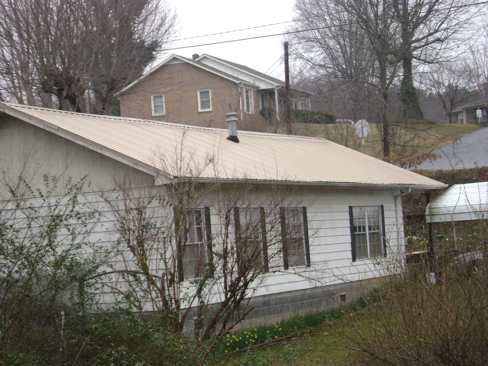Tan metal roof on a white sided house set into a hillside — Commercial Roofing by Roofing Brothers in Molena